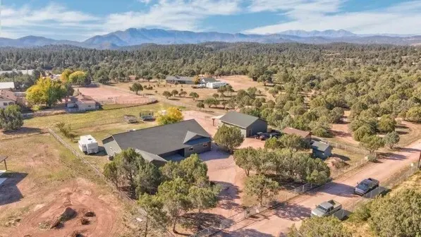 Aerial view of a rural Star Valley property with a home, fenced areas and outbuildings, with mountains in the distance