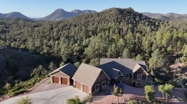 Aerial view of a large home with a three-car garage in pine forest with mountains beyond, Star Valley, Arizona